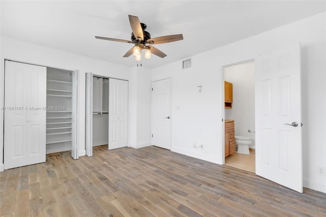 unfurnished bedroom with ceiling fan, multiple closets, ensuite bath, and light hardwood / wood-style floors