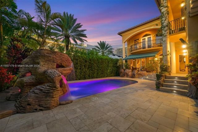 pool at dusk featuring pool water feature and a patio area