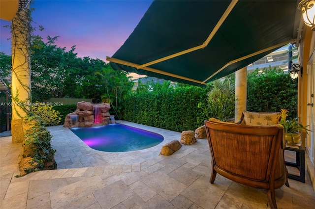 pool at dusk with a patio and pool water feature