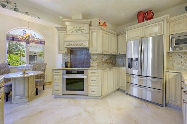 9580 Byron Ave, Surfside, FL 33154 - kitchen with cream cabinets, appliances with stainless steel finishes, a chandelier, light stone countertops, and decorative backsplash