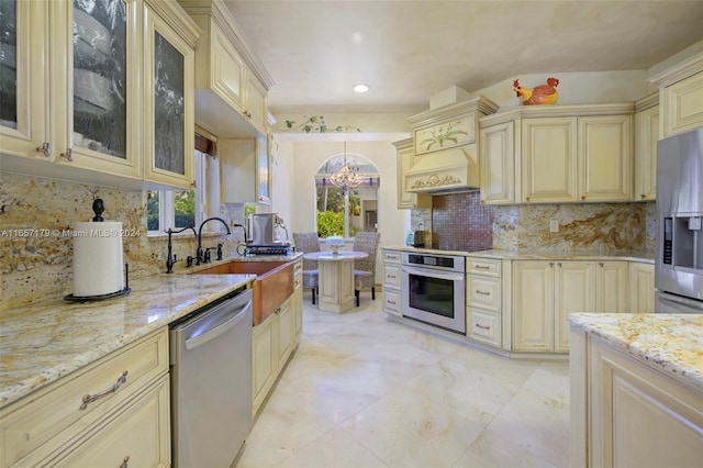 kitchen featuring hanging light fixtures, light stone counters, stainless steel appliances, cream cabinets, and a chandelier