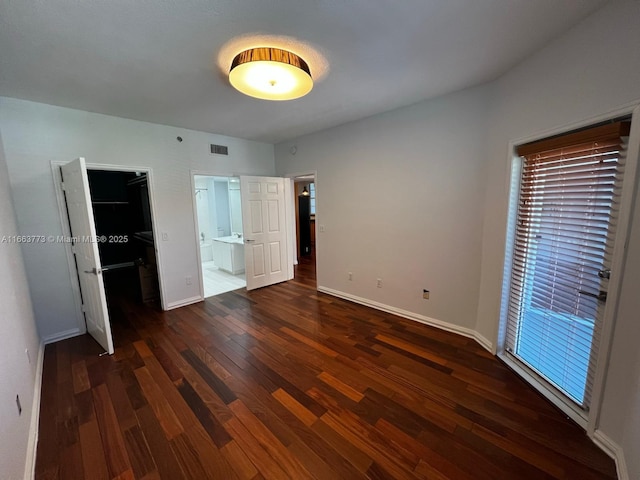 unfurnished bedroom with ensuite bathroom, dark hardwood / wood-style floors, and a spacious closet