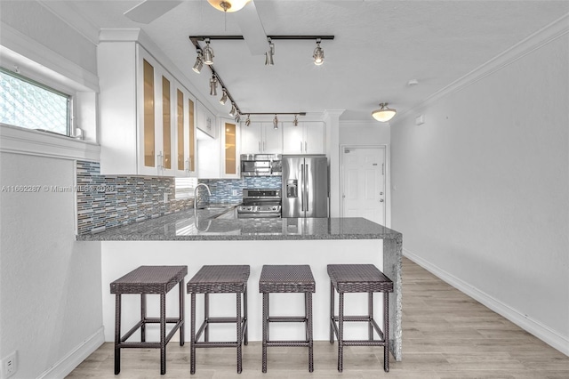 kitchen featuring stainless steel appliances, a peninsula, light wood-style floors, tasteful backsplash, and dark stone countertops