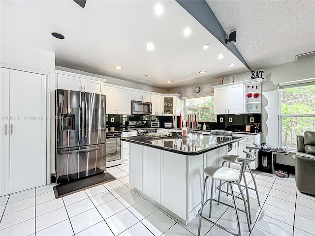 kitchen featuring stainless steel appliances, white cabinets, a center island, and backsplash