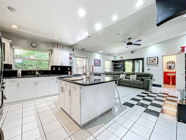 kitchen with a textured ceiling, a center island, light tile patterned flooring, white cabinets, and ceiling fan