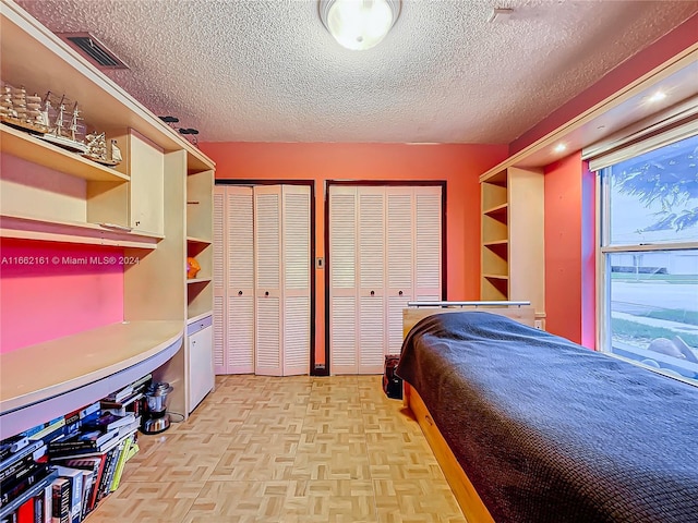 bedroom with a textured ceiling, two closets, and light parquet floors