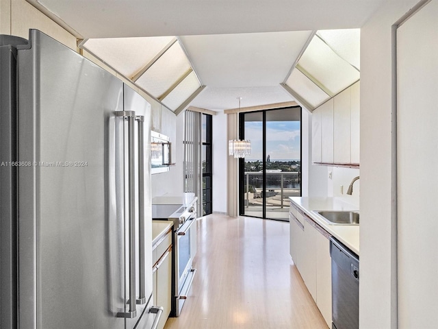 kitchen with light hardwood / wood-style floors, sink, floor to ceiling windows, white cabinets, and stainless steel appliances