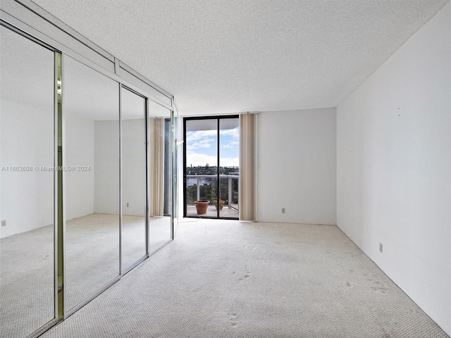 unfurnished bedroom featuring a textured ceiling, a wall of windows, and light colored carpet