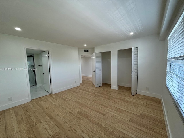 unfurnished bedroom featuring light wood-type flooring, two closets, and ensuite bath