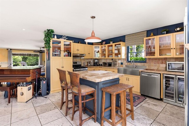 kitchen featuring a kitchen island, butcher block counters, sink, beverage cooler, and stainless steel appliances