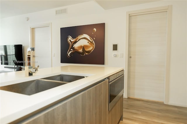 kitchen with light hardwood / wood-style flooring, stainless steel microwave, and sink