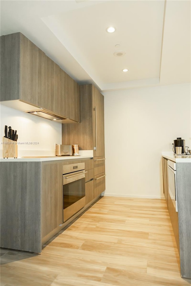 kitchen with light hardwood / wood-style floors, stainless steel oven, and a tray ceiling