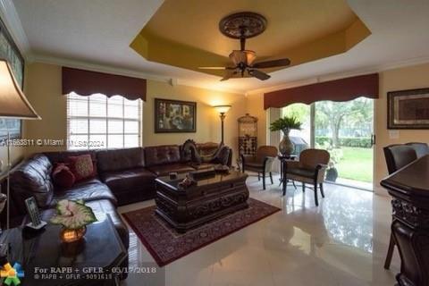 living room with a healthy amount of sunlight, a tray ceiling, ceiling fan, and ornamental molding