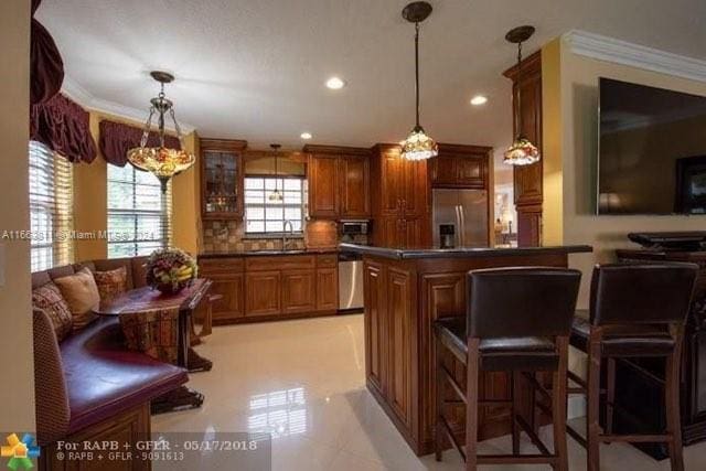 kitchen with ornamental molding, a chandelier, appliances with stainless steel finishes, a kitchen breakfast bar, and a center island