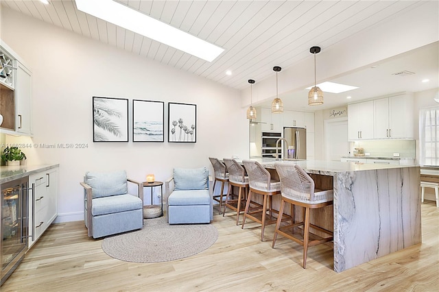 kitchen featuring stainless steel appliances, light hardwood / wood-style flooring, pendant lighting, a breakfast bar, and white cabinets