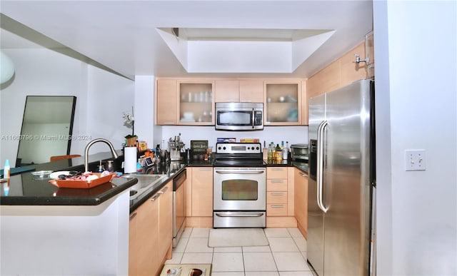 kitchen with light brown cabinets, kitchen peninsula, stainless steel appliances, and light tile patterned floors