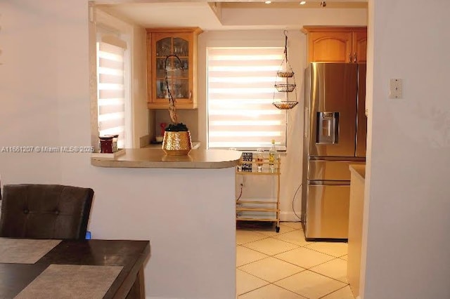 kitchen featuring light tile patterned flooring, a peninsula, glass insert cabinets, and stainless steel refrigerator with ice dispenser