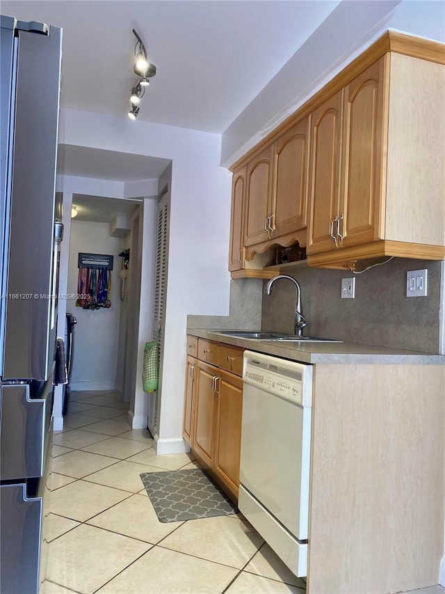 kitchen featuring light tile patterned floors, white dishwasher, freestanding refrigerator, a sink, and decorative backsplash