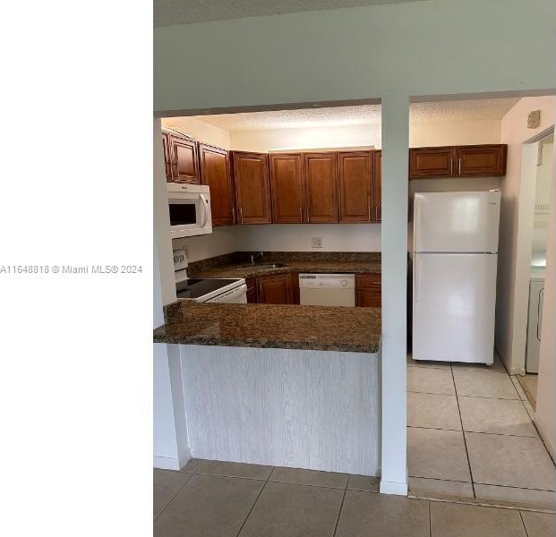 kitchen featuring light tile patterned floors, dark countertops, a peninsula, and white appliances