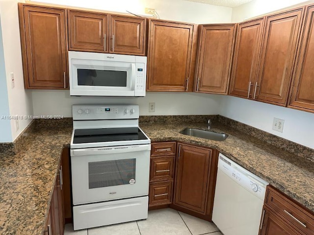 kitchen featuring white appliances, dark stone countertops, sink, and light tile patterned floors