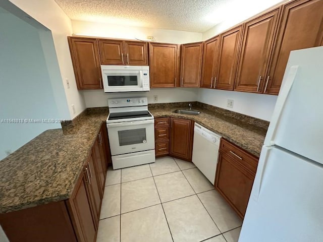 kitchen featuring kitchen peninsula, light tile patterned floors, white appliances, a textured ceiling, and dark stone countertops