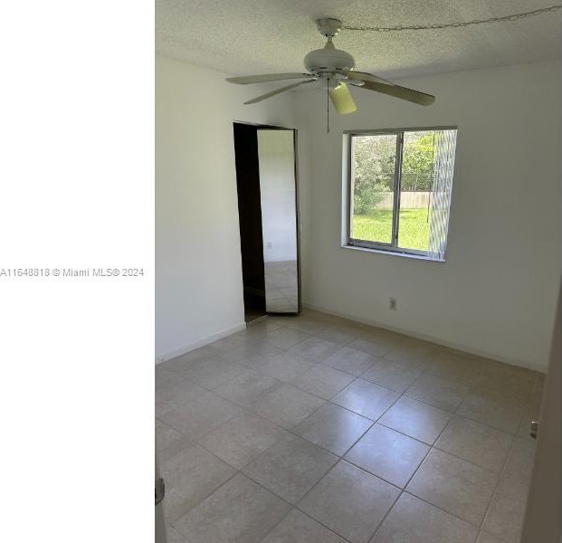 tiled empty room with ceiling fan and a textured ceiling