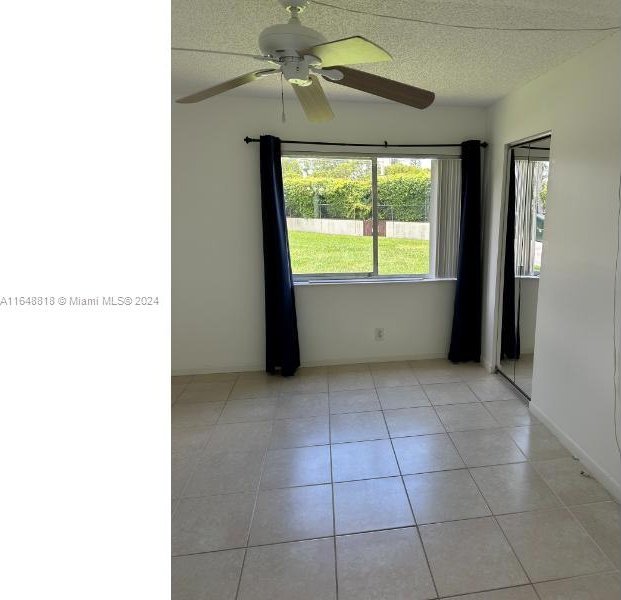 spare room with a textured ceiling, light tile patterned floors, and ceiling fan