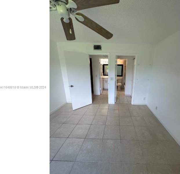 empty room with ceiling fan, light tile patterned flooring, and a textured ceiling