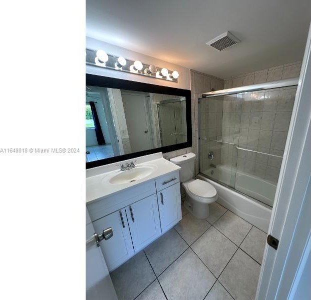 bathroom featuring visible vents, tile patterned floors, vanity, combined bath / shower with glass door, and toilet
