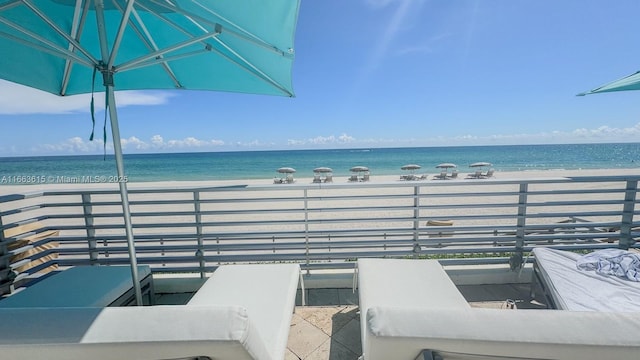 view of patio with a balcony, an outdoor living space, a water view, and a view of the beach