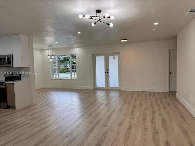 unfurnished living room with a textured ceiling, light wood-type flooring, an inviting chandelier, and french doors