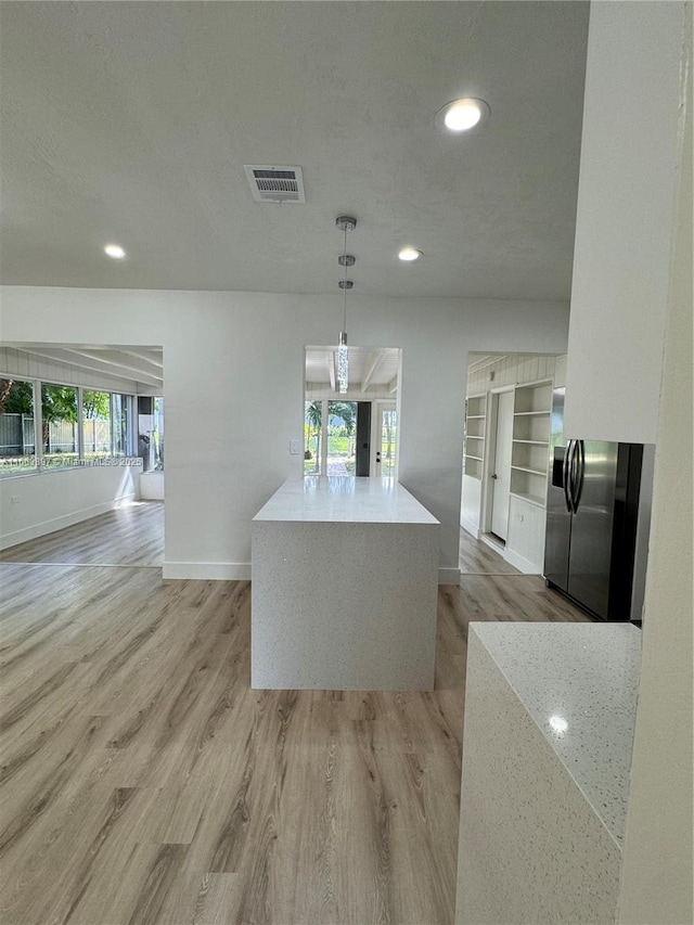 kitchen featuring decorative light fixtures, a kitchen island, light wood-type flooring, and a wealth of natural light