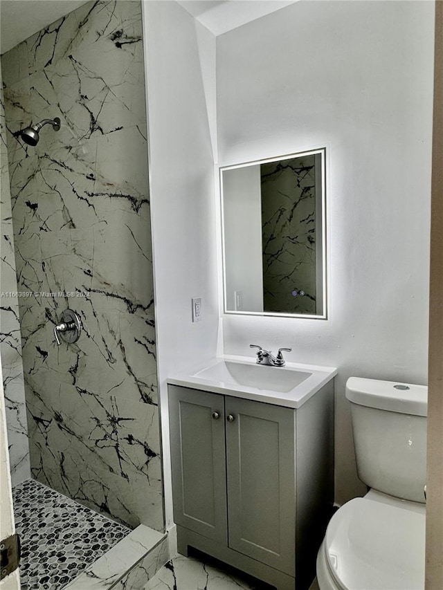 bathroom with a tile shower, vanity, and toilet