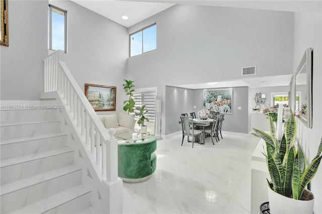 interior space featuring marble finish floor, visible vents, a towering ceiling, and baseboards