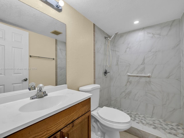 bathroom with a textured ceiling, tiled shower, vanity, and toilet