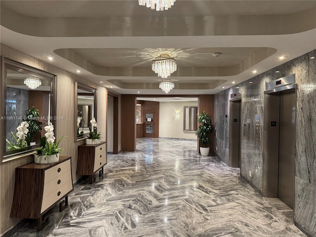 corridor with a tray ceiling, elevator, and a chandelier