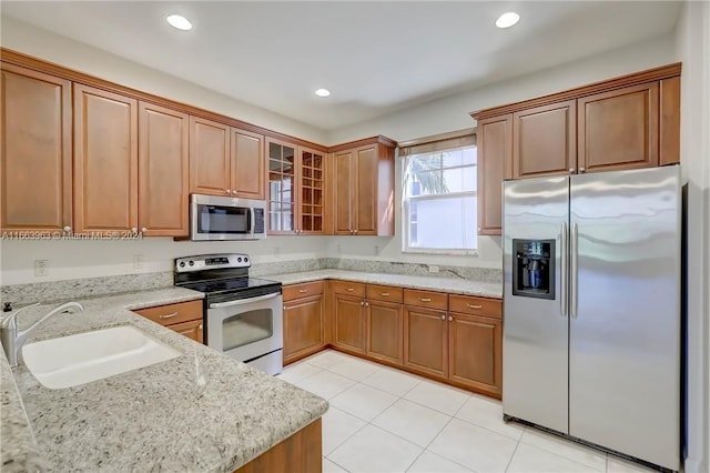 kitchen with light stone counters, appliances with stainless steel finishes, light tile patterned flooring, and sink