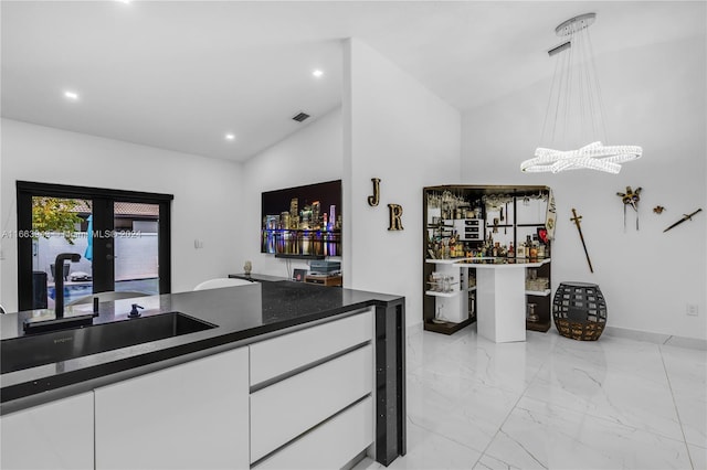 kitchen with sink, white cabinetry, vaulted ceiling, decorative light fixtures, and french doors