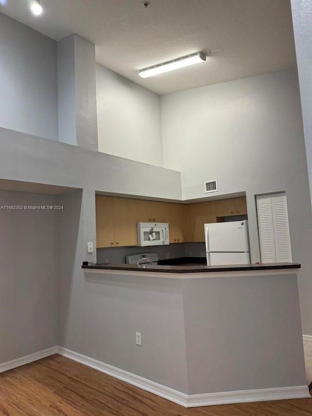 kitchen featuring light hardwood / wood-style floors, white appliances, a high ceiling, and kitchen peninsula