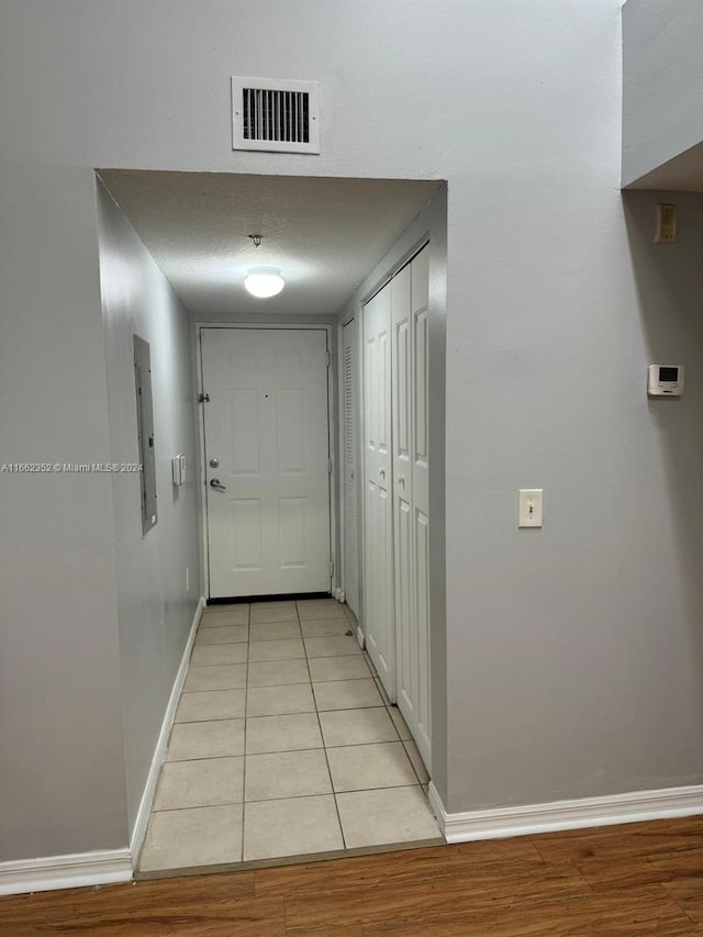 hallway featuring electric panel, light tile patterned floors, and a textured ceiling