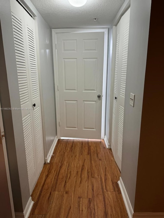 corridor with a textured ceiling and hardwood / wood-style floors