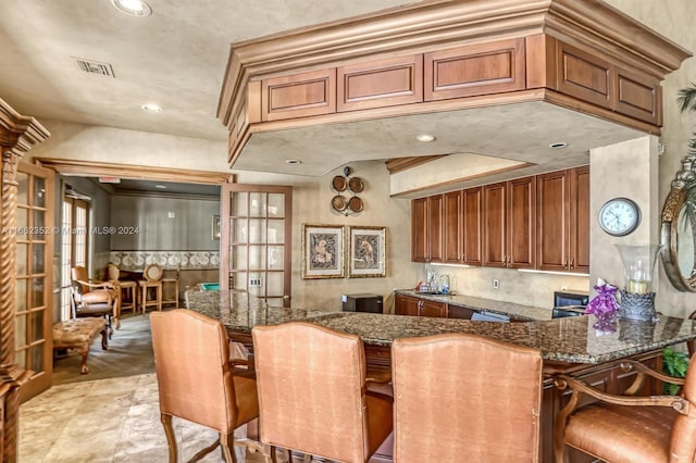 kitchen with kitchen peninsula, dark stone countertops, and a breakfast bar