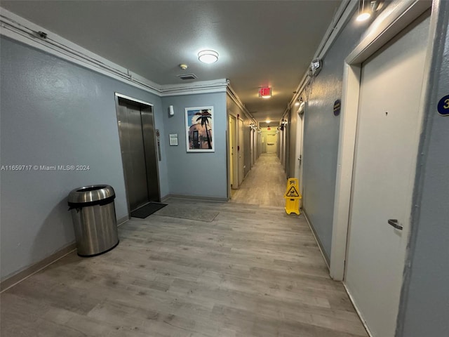 corridor with light hardwood / wood-style flooring, ornamental molding, and elevator