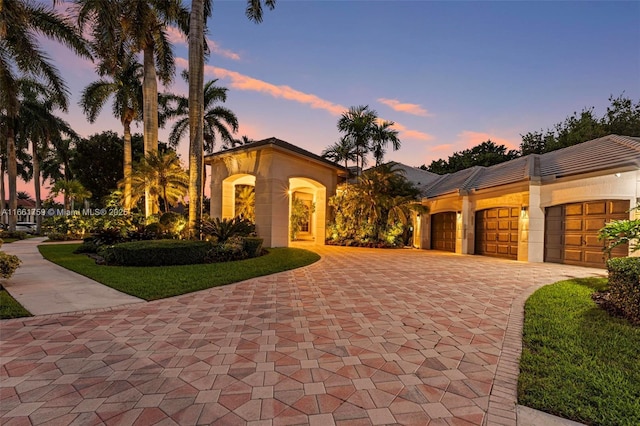 mediterranean / spanish-style home with a tiled roof, a garage, decorative driveway, and stucco siding