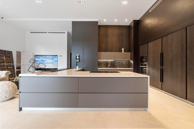 kitchen with dark brown cabinetry, light tile patterned flooring, a large island with sink, oven, and decorative backsplash