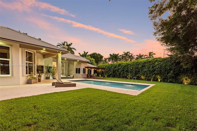 pool at dusk with a lawn, a patio, and pool water feature