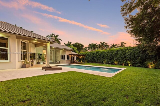 pool at dusk with a deck, a lawn, and pool water feature