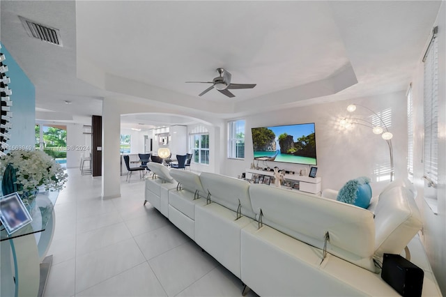 tiled living room featuring ceiling fan with notable chandelier and a raised ceiling