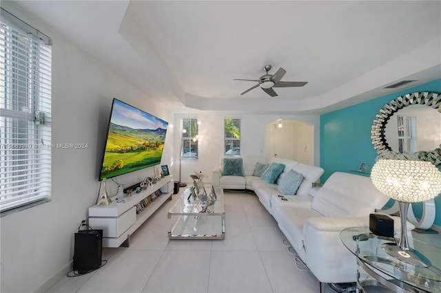 living room featuring ceiling fan with notable chandelier, a tray ceiling, and light tile patterned floors