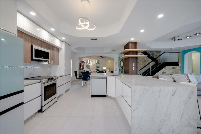 kitchen featuring ceiling fan with notable chandelier, white cabinets, stainless steel appliances, a raised ceiling, and decorative light fixtures